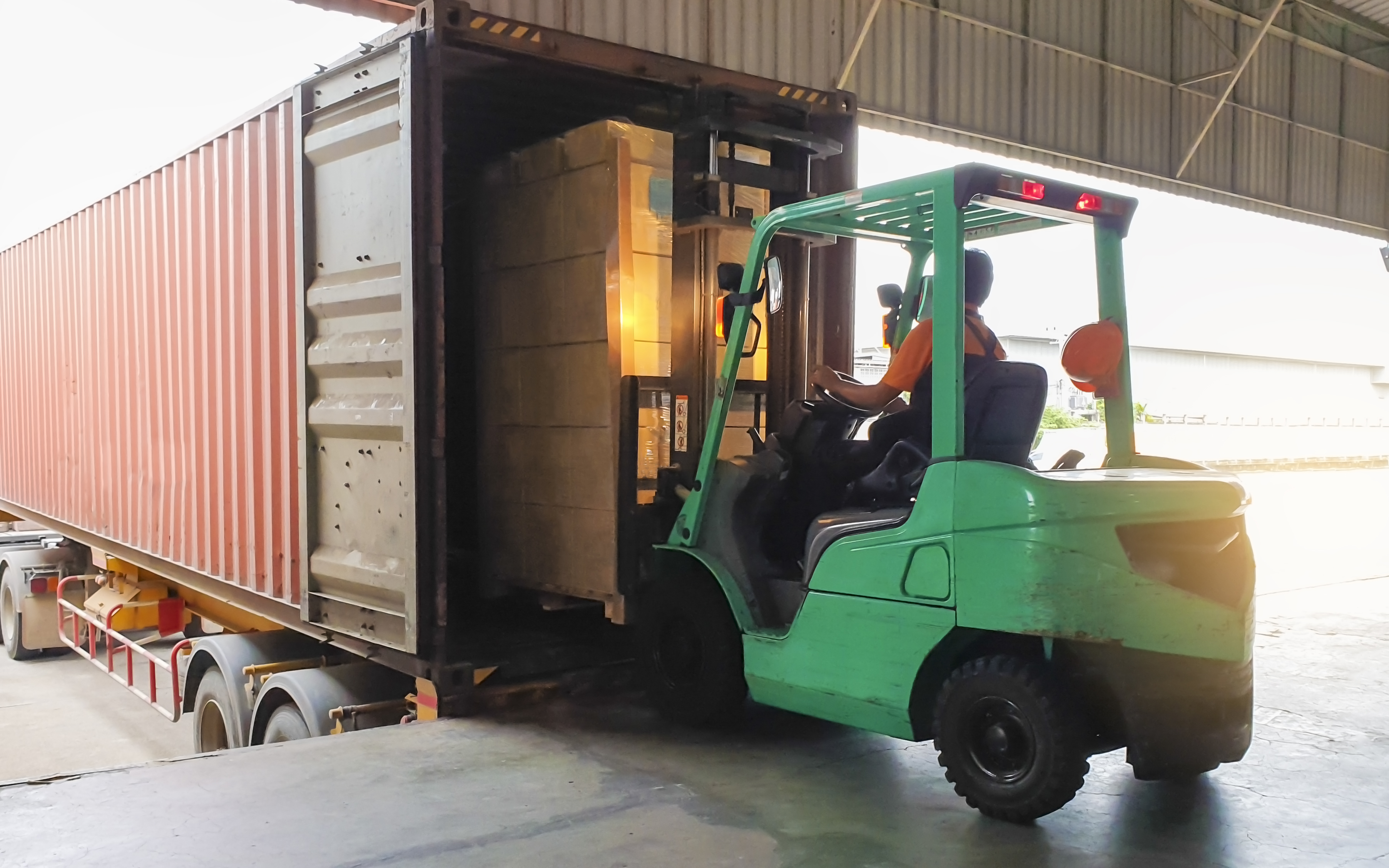 Forklift driver loading goods pallet into the truck container