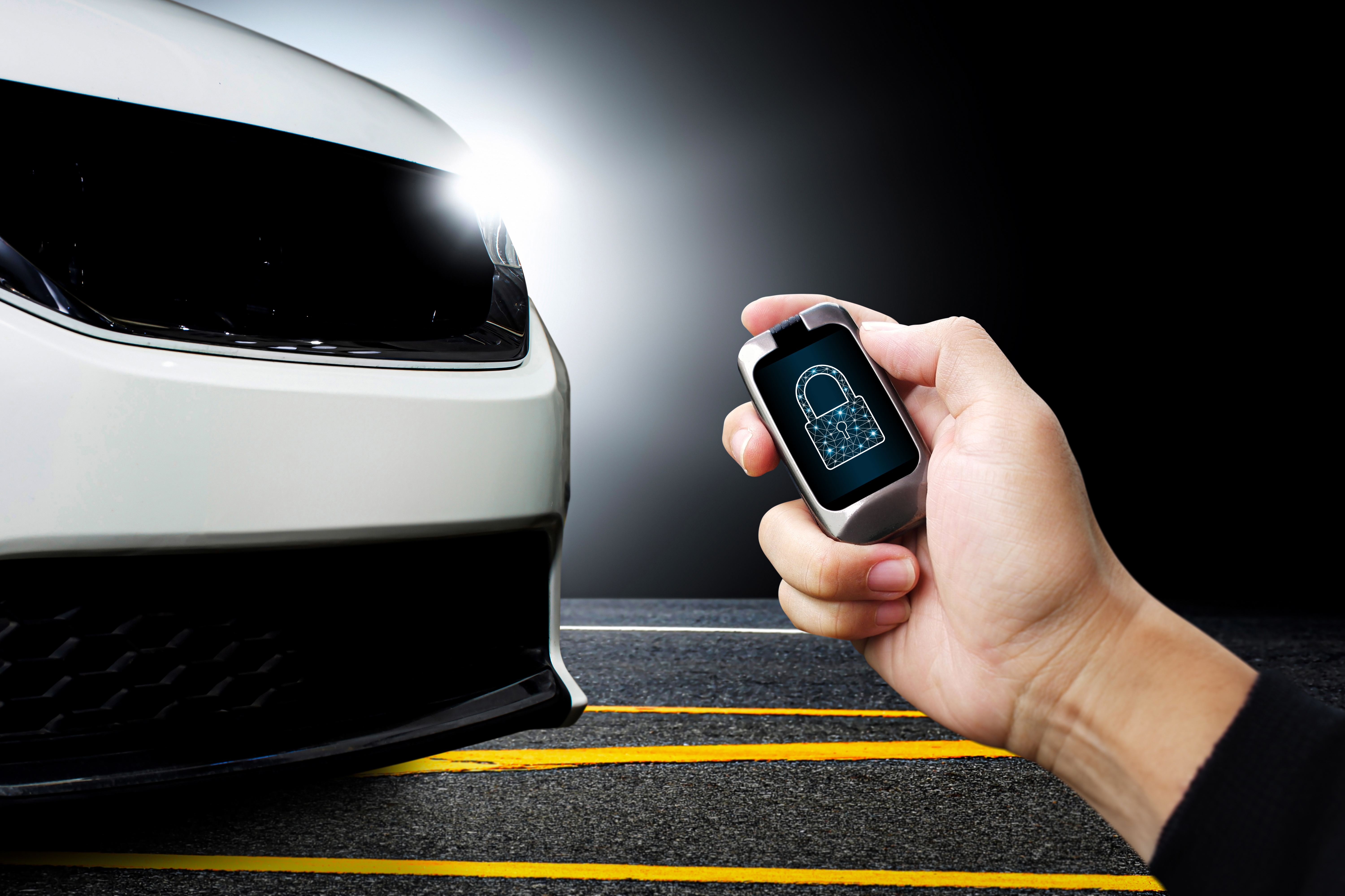 Driver hand holds keyless remote with key locked icon on display with white modern car parked on the road in the background - stock photo