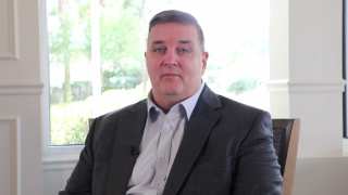 A man in a suit sits in front of a window.